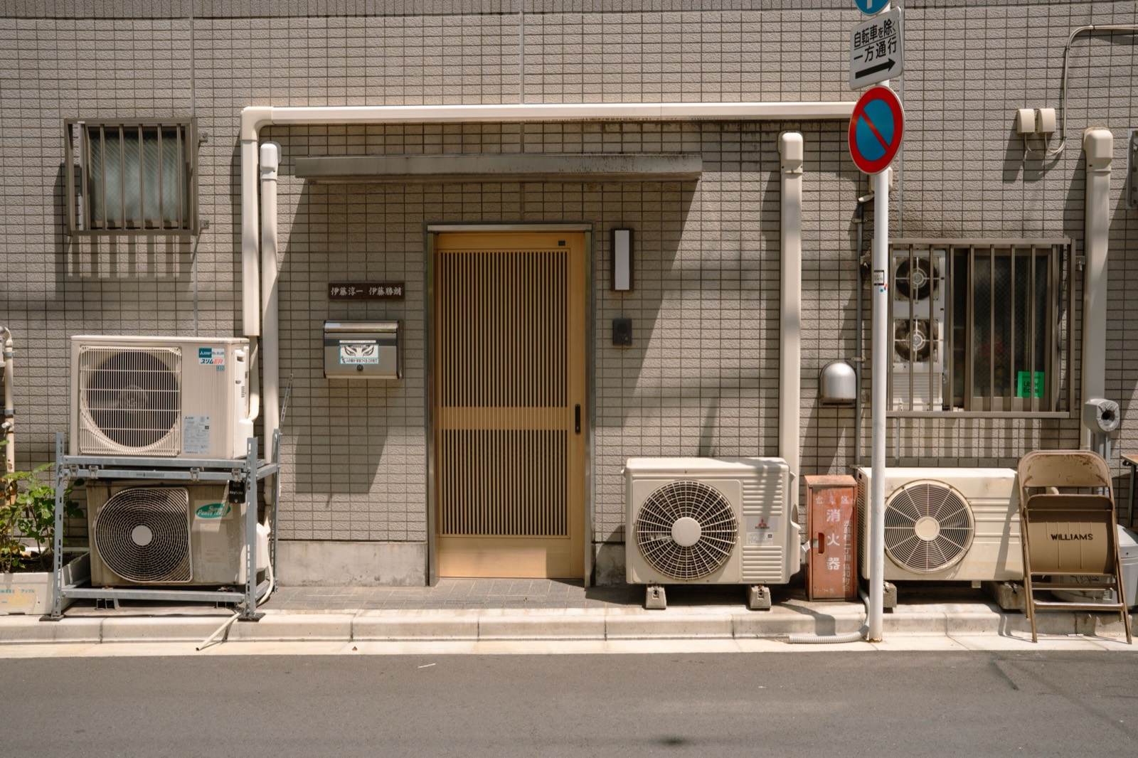 Mini-split condenser units installed at street level outside a tiled building, with line sets routed along the wall